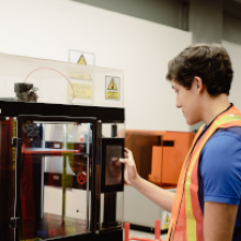 Carrera de Ingeniería Industrial UDLA Estudiante frente a una impresora 3D simulando procesos